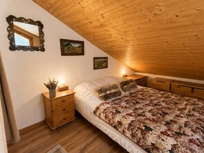 A bedroom with a sloped ceiling, wooden headboard, a bed with a floral-patterned bedspread, two wall-mounted paintings, a bedside table with a lamp, and a mirror with a floral frame. - Spacious duplex, mountain view - 5 guests (Méribel)
