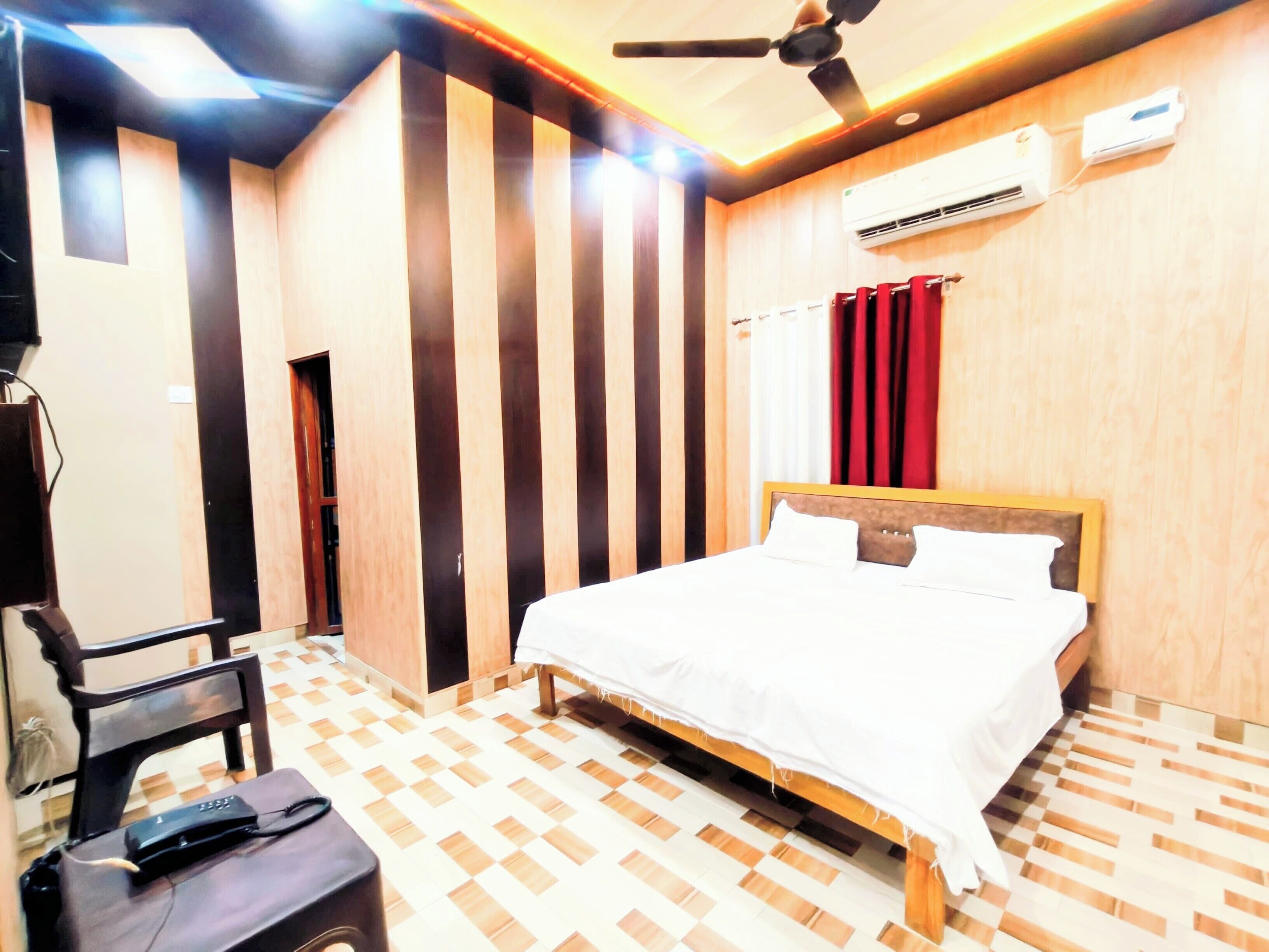Habitación de hotel con cama, una silla, escritorio, equipo de aire acondicionado y ventilador de techo.