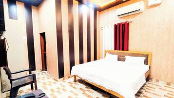 Habitación de hotel con cama, una silla, escritorio, equipo de aire acondicionado y ventilador de techo.