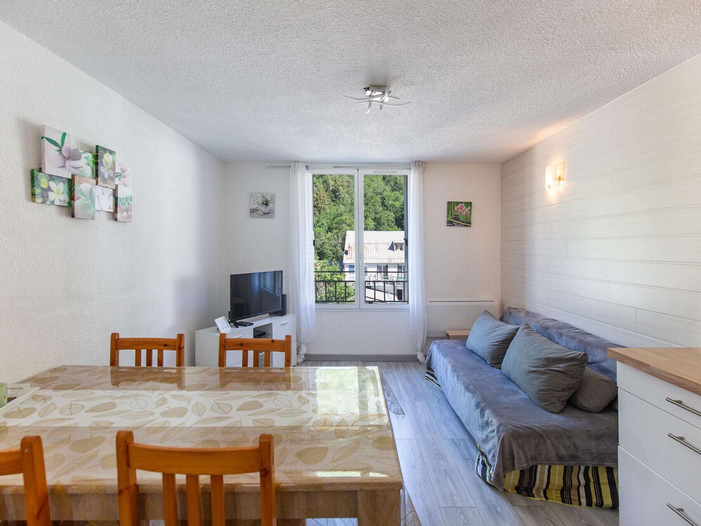 A compact living space with a dining table, chairs, a sofa, a TV, and artwork on the walls.