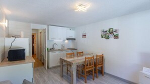 A compact living space with a kitchenette, a dining area with a wooden table and chairs, and a small seating area with a sofa. - Comfortable central studio - 4 guests (Barèges)