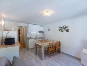 Ein kompakter Wohnbereich mit Küchenzeile, einem Essbereich mit Holztisch und Stühlen sowie einer kleinen Sitzecke mit einer Couch.