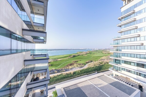 Un edificio moderno con fachada de vidrio, terraza en la azotea y vistas a un campo de golf y al agua.
