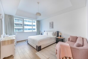 Habitación de hotel moderna con una cama grande, mesitas de noche, una silla y vistas a la ciudad.