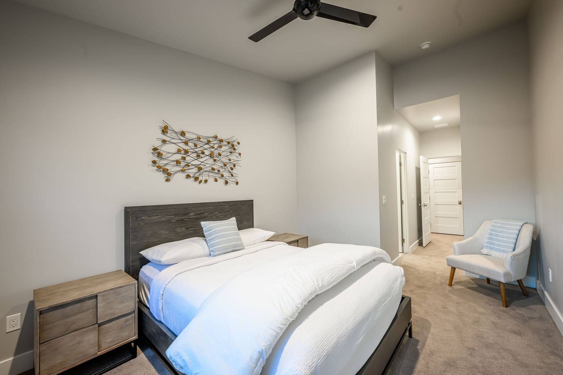 A bedroom with a bed, a nightstand, a chair, a ceiling fan, and a wall art piece.
