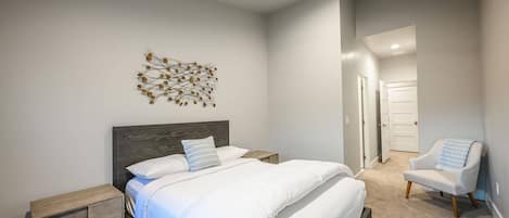 A bedroom with a bed, a nightstand, a chair, a ceiling fan, and a wall art piece.