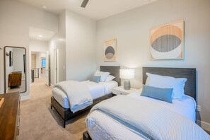 Quarto de hotel com duas camas, mesa de cabeceira com abajur, espelho e obras de arte nas paredes.