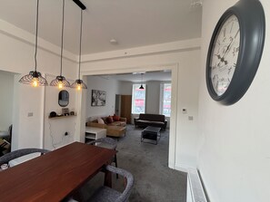 A modern living room with a dining area, a large wall clock, and a view through an open door. - Amazing Huge 5 Bed / 10 Sleeper in London Zone 2. (London)