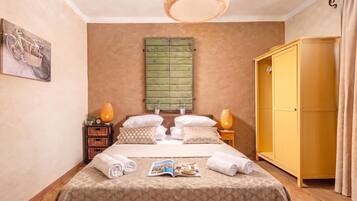 A neatly arranged bedroom with a bed, a wardrobe, a bedside table with a lamp, and a wall-mounted shelf.