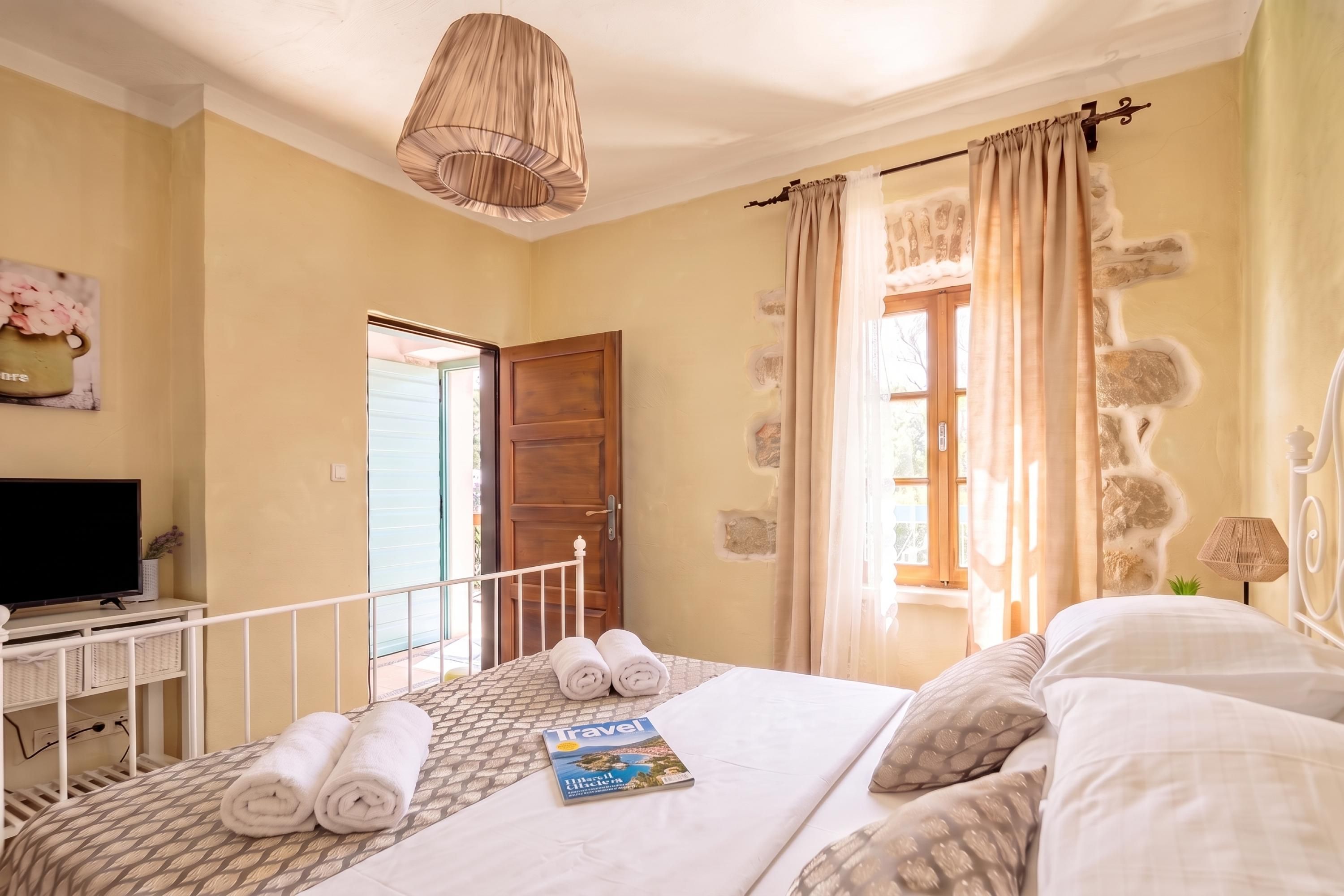 Una camera d'albergo con un letto, una televisione su un mobile, una rivista sul letto e una finestra con tende.