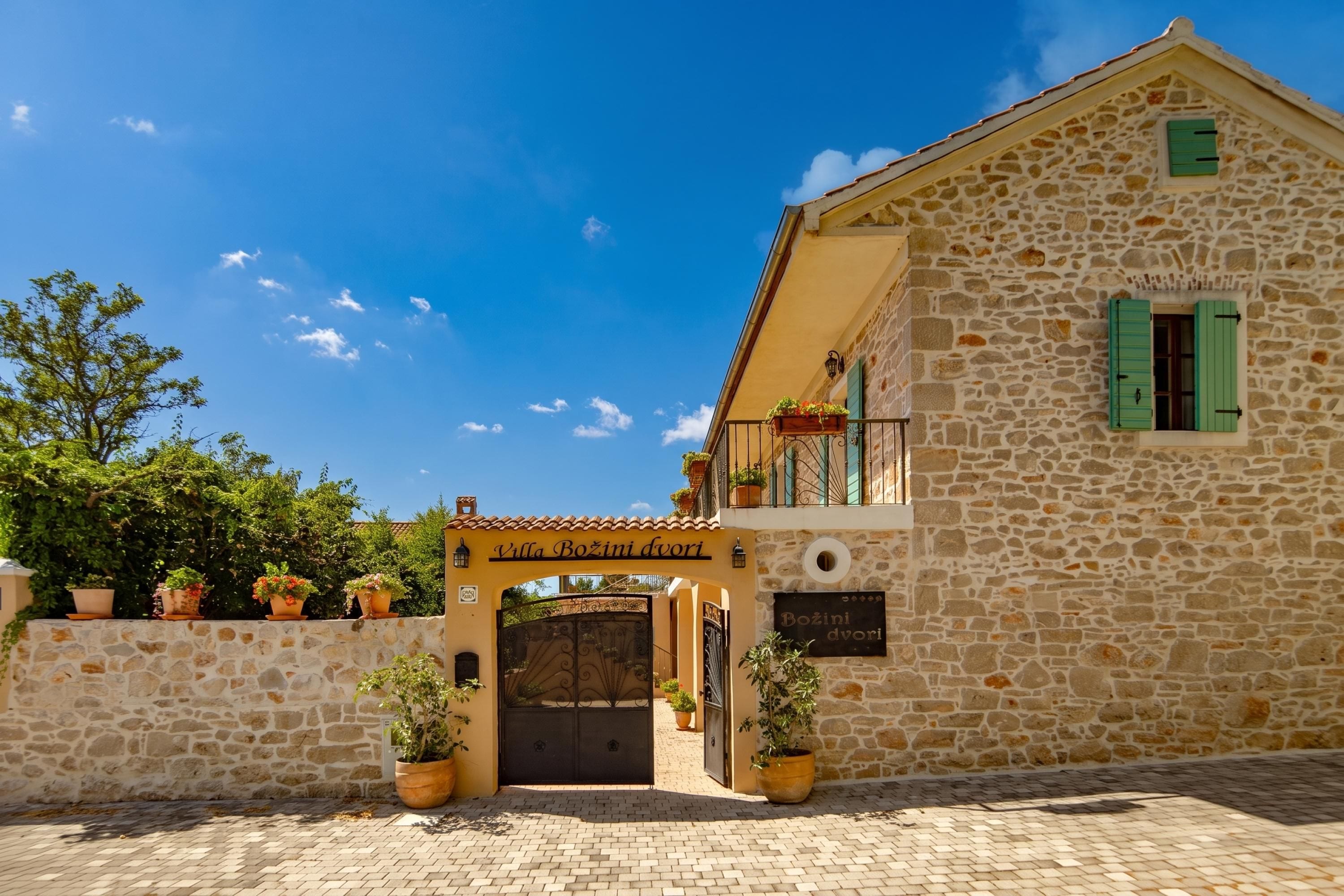 A stone building with a sign reading 'Villa Bozini dviri' and a gated entrance.