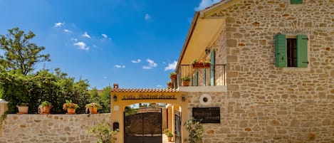 Edificio de piedra con un letrero que dice 'Villa Bozini dviri' y una entrada protegida por una reja.