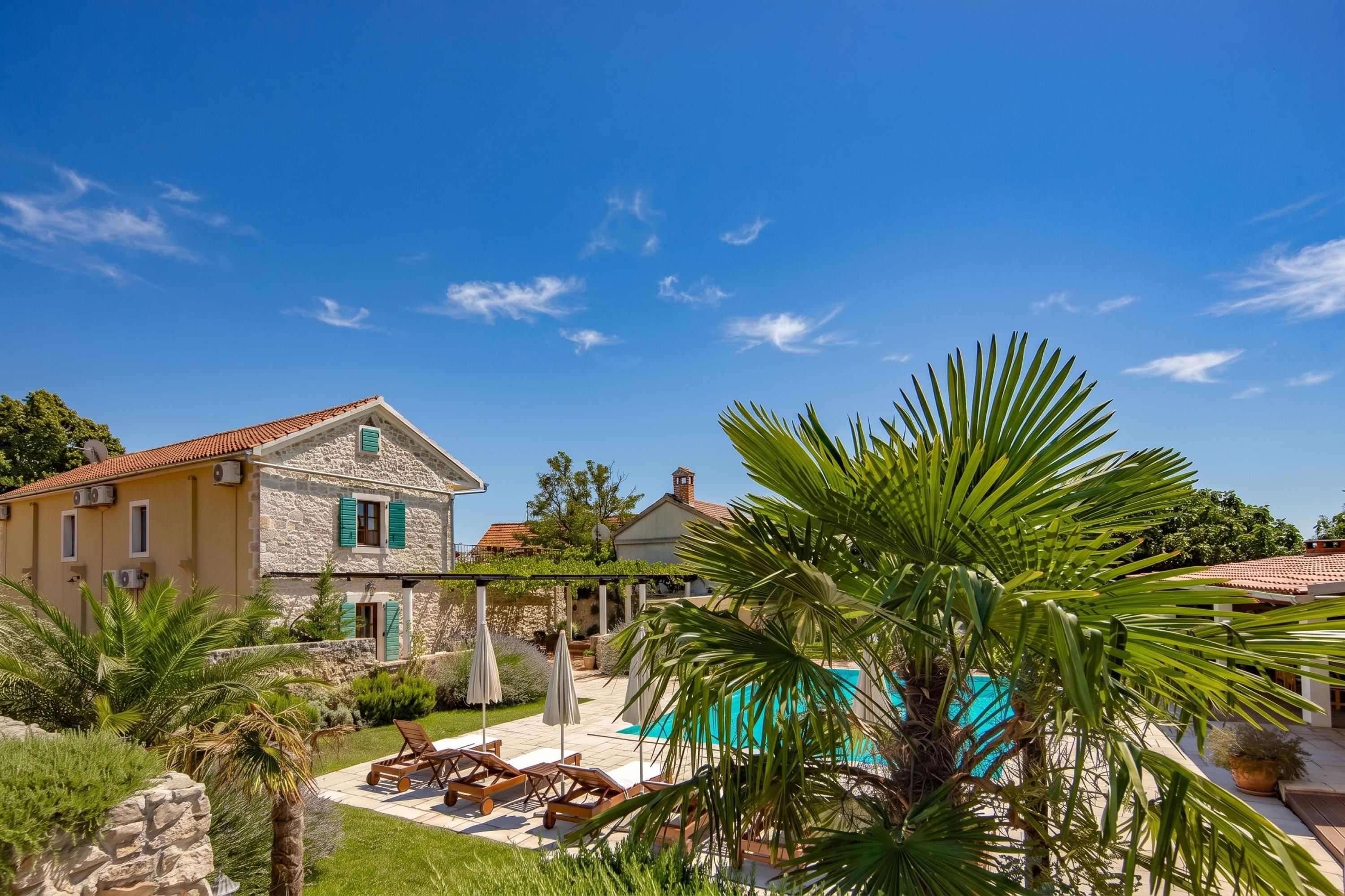 A stone house with a tiled roof, a swimming pool, and outdoor seating.