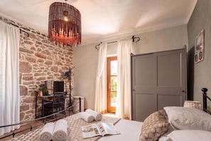 A bedroom with a stone wall, a bed with rolled towels, a TV, and a hanging light fixture. - Villa Dalmatia Luxury Stone Villa With Pool & Tennis (Sveti Filip i Jakov)