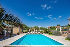 A rectangular swimming pool with a tiled deck, surrounded by lounge chairs and umbrellas, set against a clear blue sky. - Villa Dalmatia Luxury Stone Villa With Pool & Tennis (Sveti Filip i Jakov)