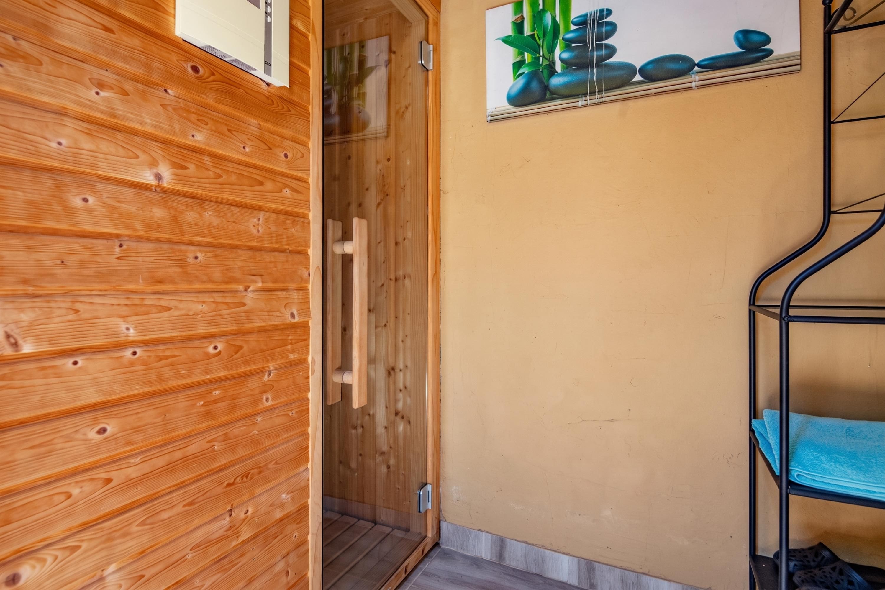 A wooden sauna room with a wooden door, a towel rack, and a wall-mounted shelf with a plant.