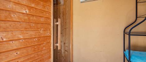 A wooden sauna room with a wooden door, a towel rack, and a wall-mounted shelf with a plant.