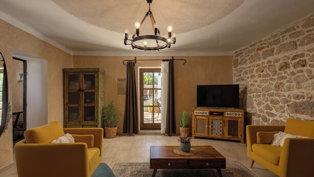 A living room with yellow sofas, a coffee table, a television, and a stone wall. - Villa Dalmatia Luxury Stone Villa With Pool & Tennis (Sveti Filip i Jakov)