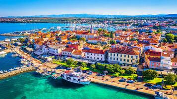 A coastal town with a marina, buildings with red-tiled roofs, and clear turquoise waters.