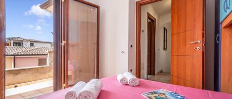 Habitación de hotel con balcón, cama con ropa de cama rosa, dos toallas enrolladas y una revista sobre la cama.