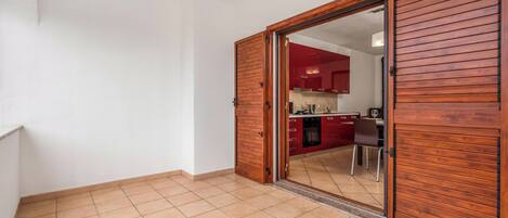 A room with a wooden door leading to a kitchen with red cabinets and a tiled floor.