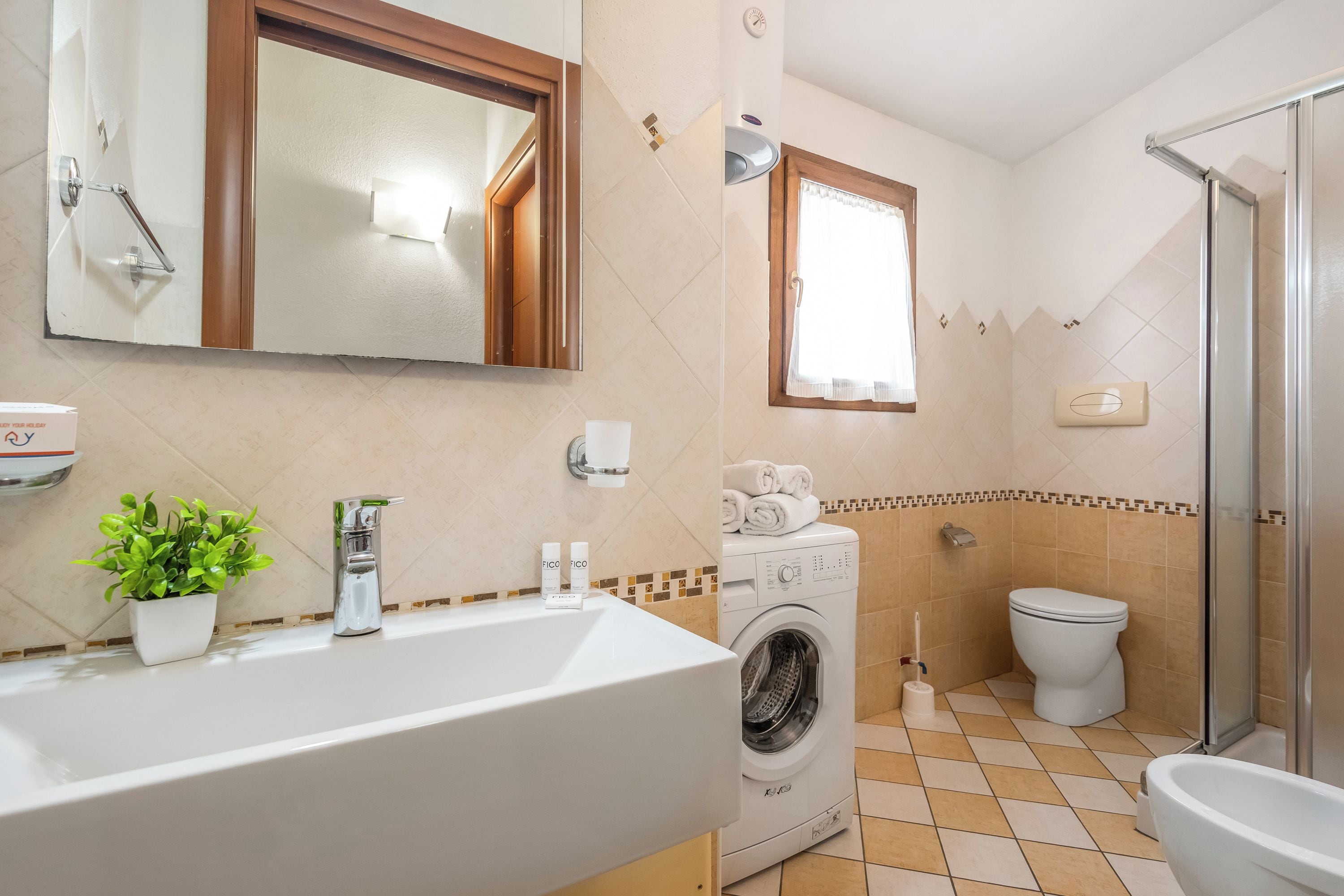 A bathroom with a sink, mirror, washing machine, toilet, and shower.