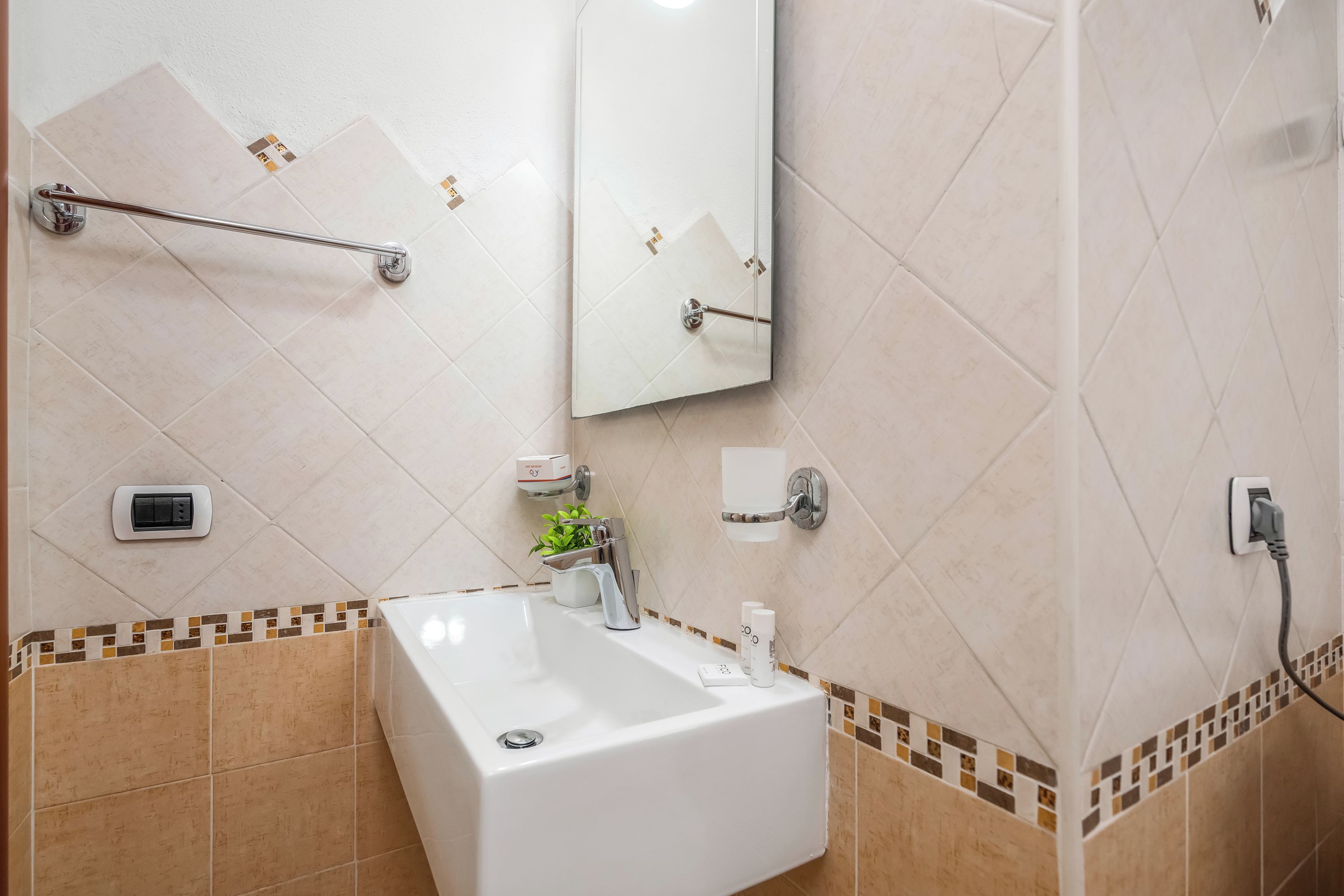 Casa de banho com lavatório branco, espelho, porta-toalhas, dispensador de sabonete e suporte para papel higiénico.