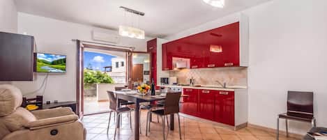 Una sala moderna con un sofá, una mesa de comedor para cuatro personas y una cocina con armarios rojos.