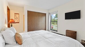 A bedroom with a bed, a window, a TV, and a door.