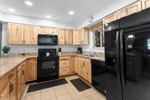 A kitchen with wooden cabinets, a black refrigerator, a microwave, and a stove. - Hi Country Haus Unit 2301 Spacious 2 bed, ground floor, walk to downtown (Winter Park)