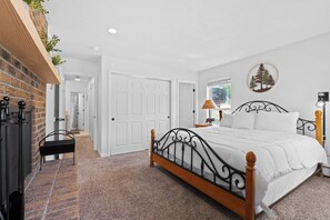 A bedroom with a wooden bed frame, white bedding, a brick wall, a bench, and a door leading to another room. - Hi Country Haus Unit 2301 Spacious 2 bed, ground floor, walk to downtown (Winter Park)