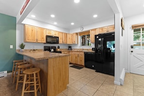 A kitchen with wooden cabinets, a black refrigerator, a microwave, and a large island with stools. - Hi Country Haus Unit 2301 Spacious 2 bed, ground floor, walk to downtown (Winter Park)