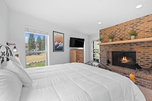 A bedroom with a large bed, a fireplace, a TV, and a view of a parking lot. - Hi Country Haus Unit 2301 Spacious 2 bed, ground floor, walk to downtown (Winter Park)