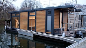 A floating houseboat with a dock, large windows, and a Yamaha outboard motor.