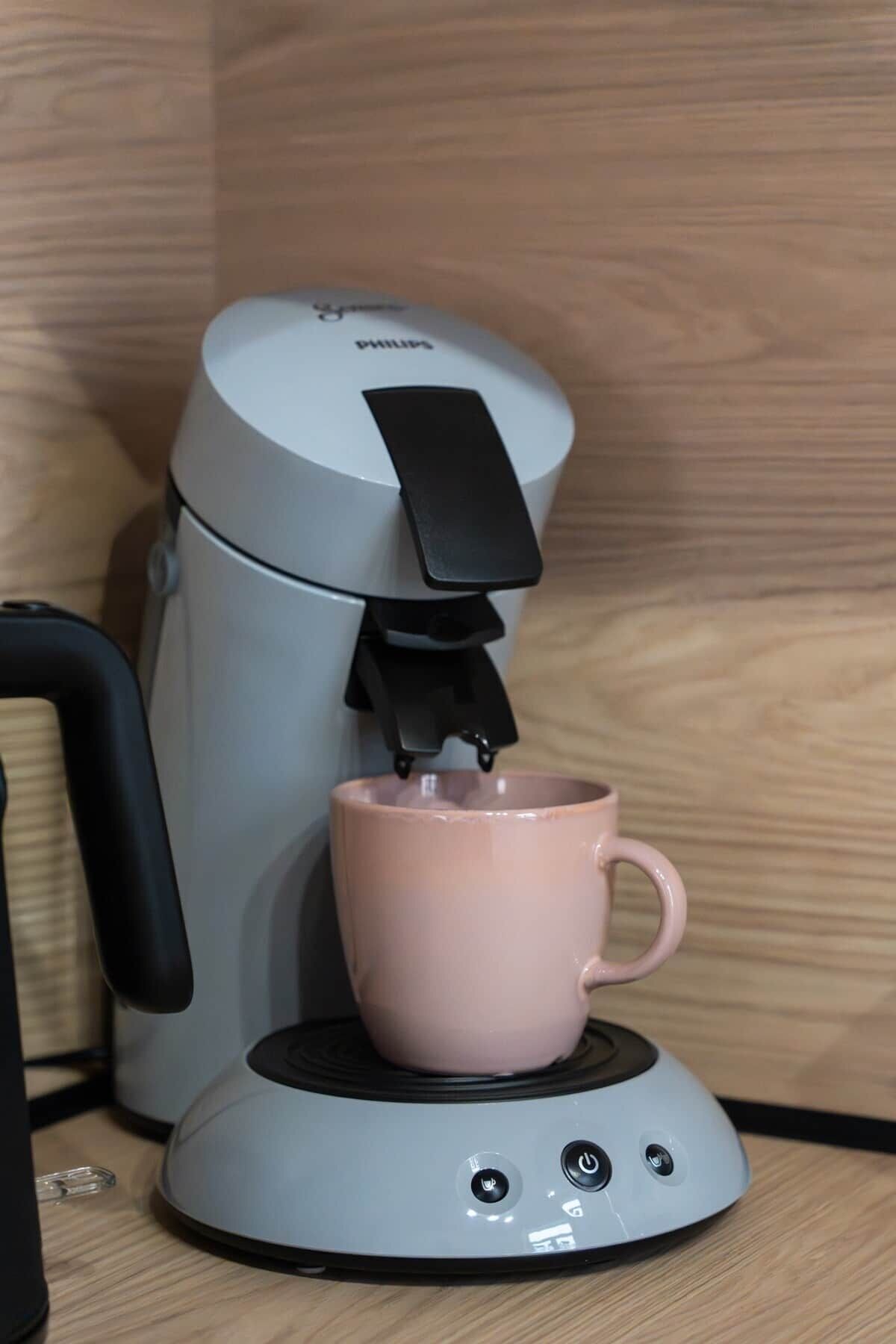 A coffee maker with a pink mug on its base.