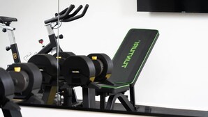 Un gimnasio con equipo de ejercicio, incluyendo una bicicleta estática, un banco y discos de pesas.