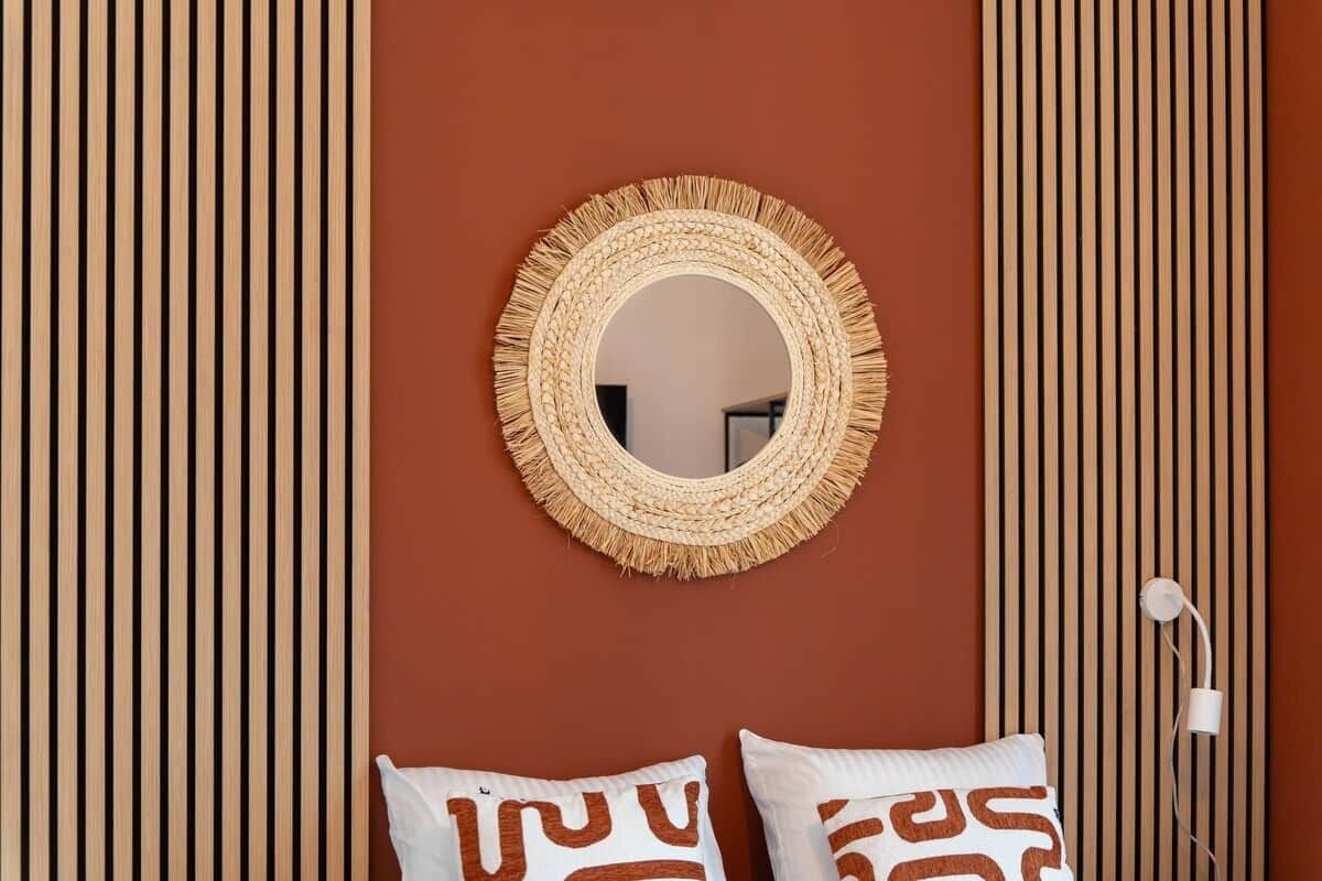 Une pièce avec un miroir à motifs tissés accroché au mur, deux coussins à motifs et un panneau décoratif en bois vertical.