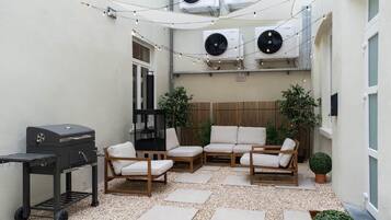 Een terras buiten met een barbecue, zithoek en lichtjes.