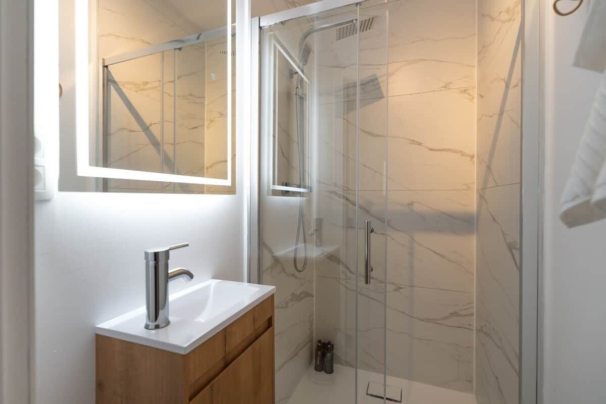 A modern bathroom with a glass-enclosed shower, a white sink, and a wooden vanity.