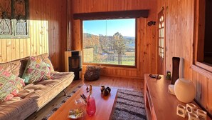 A wooden cabin interior with a sofa, coffee table, and a view through a large window.