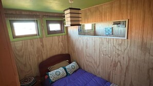 A room with a bed, a ceiling fan, and two windows.
