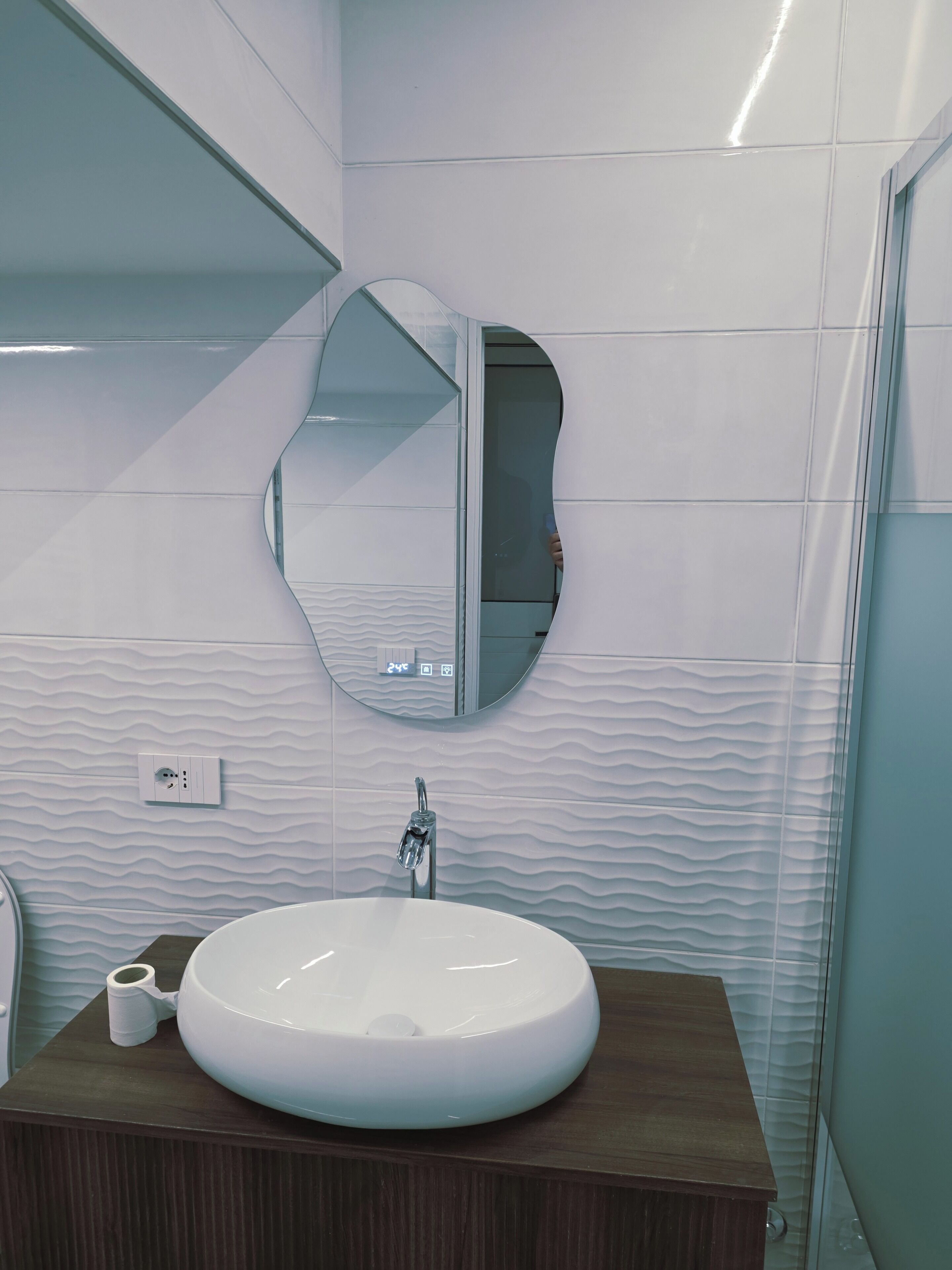 A bathroom with a white sink, a round mirror, and a wall-mounted light fixture.