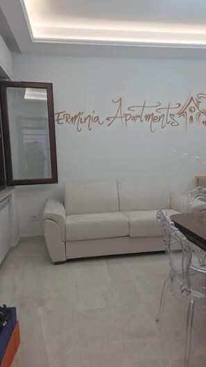 Una sala de estar con sofá, una mesa de comedor y sillas. Hay una pared con el texto 'Ermuvia Apartments' y un espejo sobre el sofá.