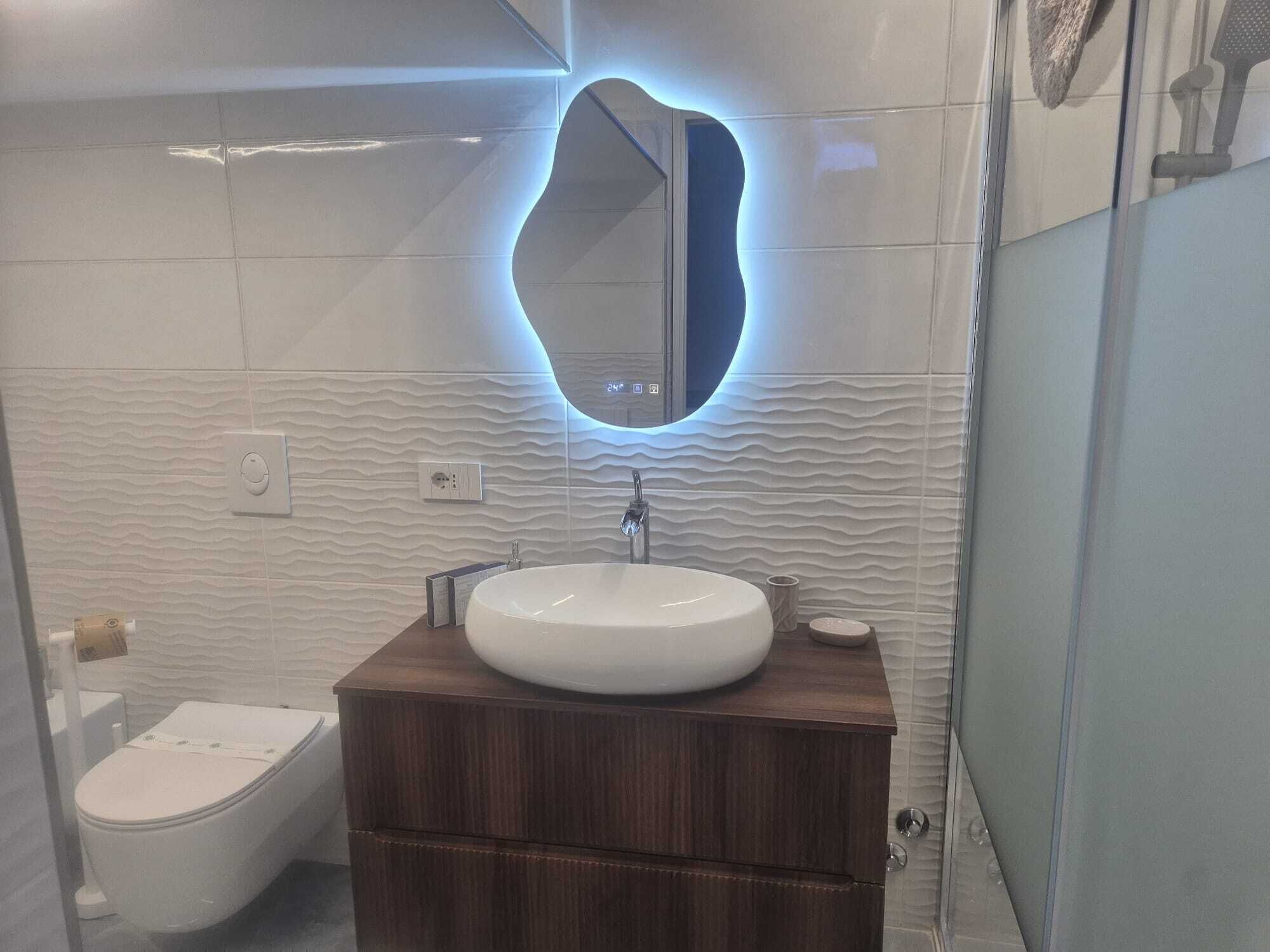 A modern bathroom with a round mirror, a white sink, and a wooden vanity.