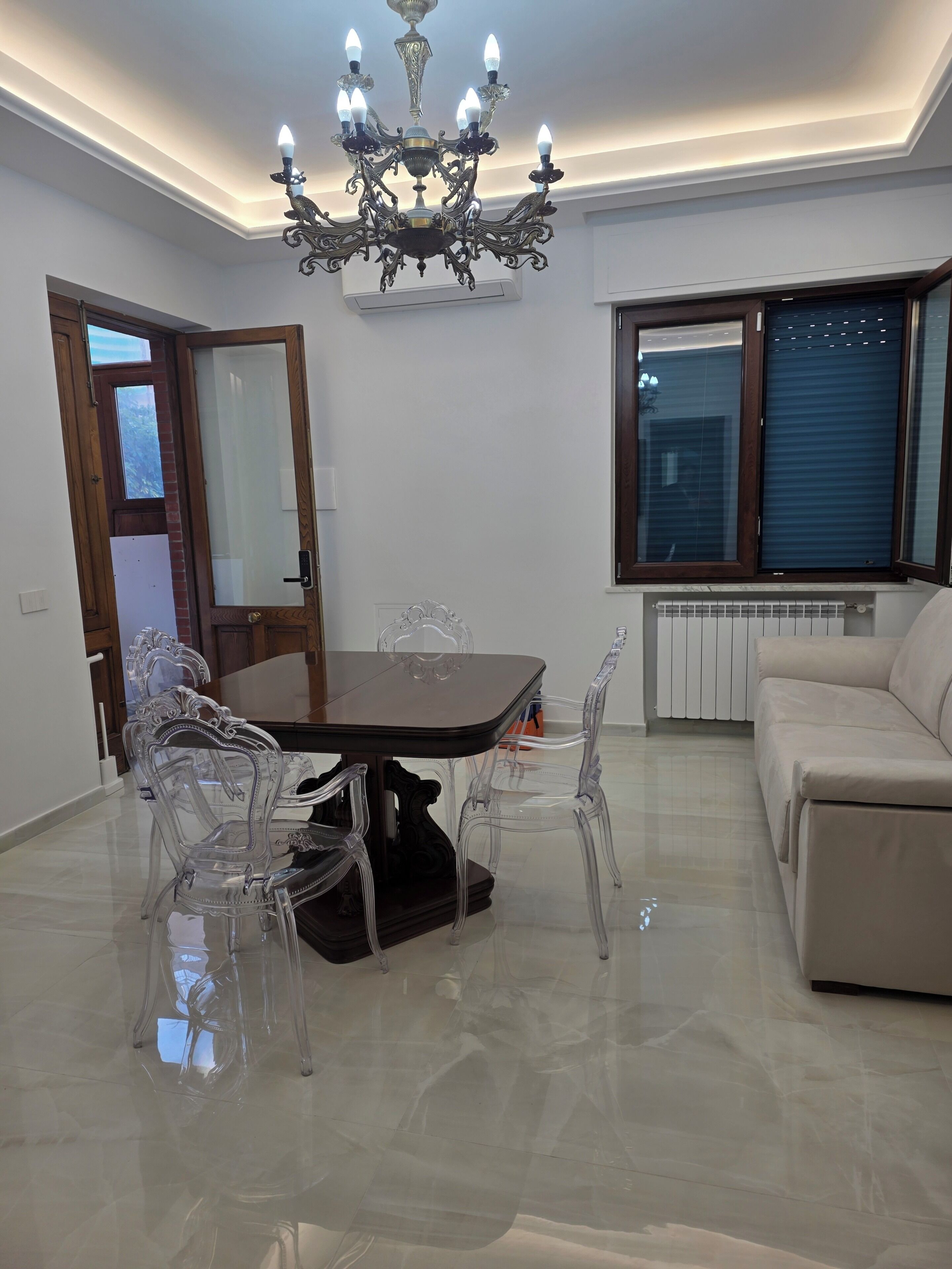 Uma sala de jantar com um candelabro, uma mesa e cadeiras transparentes.
