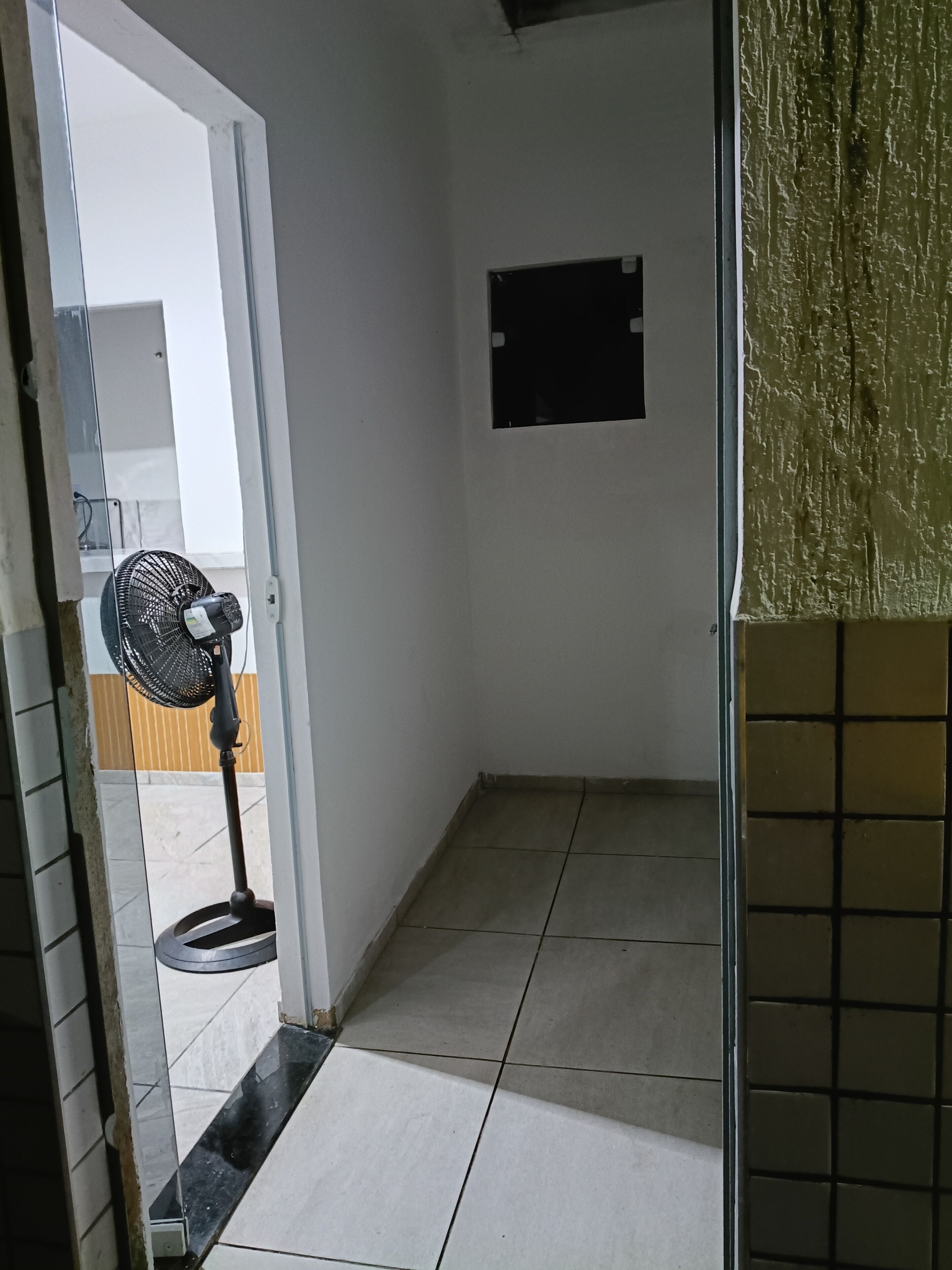 Une pièce avec un sol carrelé, un ventilateur sur pied et un tableau noir accroché au mur.