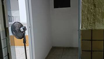 Une pièce avec un sol carrelé, un ventilateur sur pied et un tableau noir accroché au mur.
