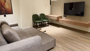 Un salon moderne comprenant un canapé, deux fauteuils, un téléviseur fixé au mur et une console en bois.