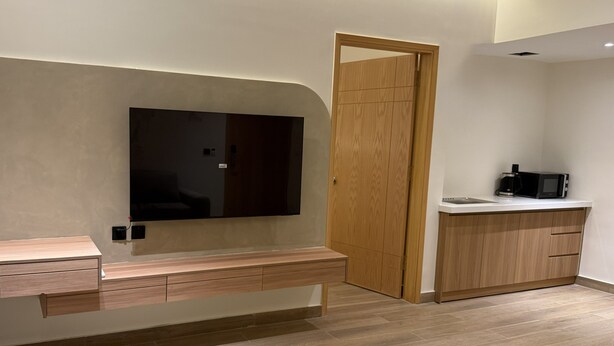 Une cuisine moderne équipée d’un four à micro-ondes encastré, de meubles en bois et d’un grand téléviseur à écran plat fixé au mur.