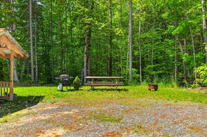Ein Picknickbereich mit Grill, Bank und einer Holzkonstruktion in einem Waldgebiet.